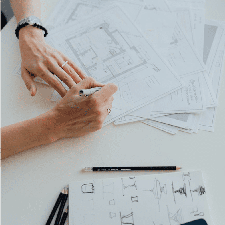 Hands writing on architectural plans with pencil and pens on a white table.